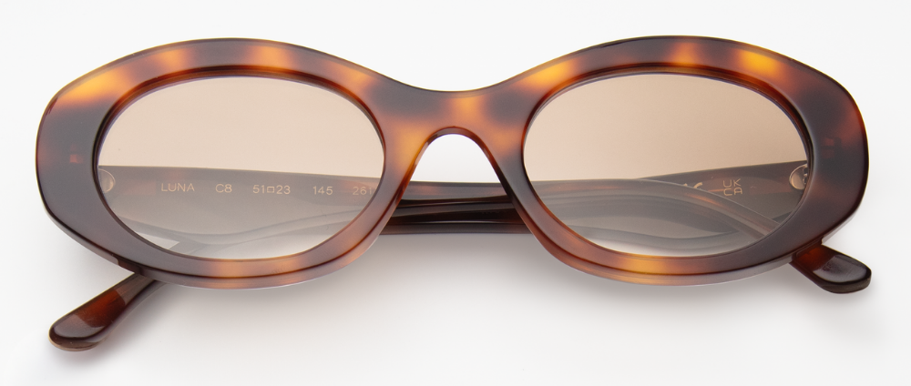 A studio product shot of the Luna sunglasses, featuring a thick acetate frame in a dark tortoise-shell pattern paired with warm tan lenses.