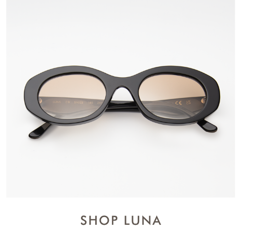 A studio product shot of the Luna sunglasses, featuring a thick black acetate rounded oval frame paired with light brown gradient lenses. Simple text below reads, 
