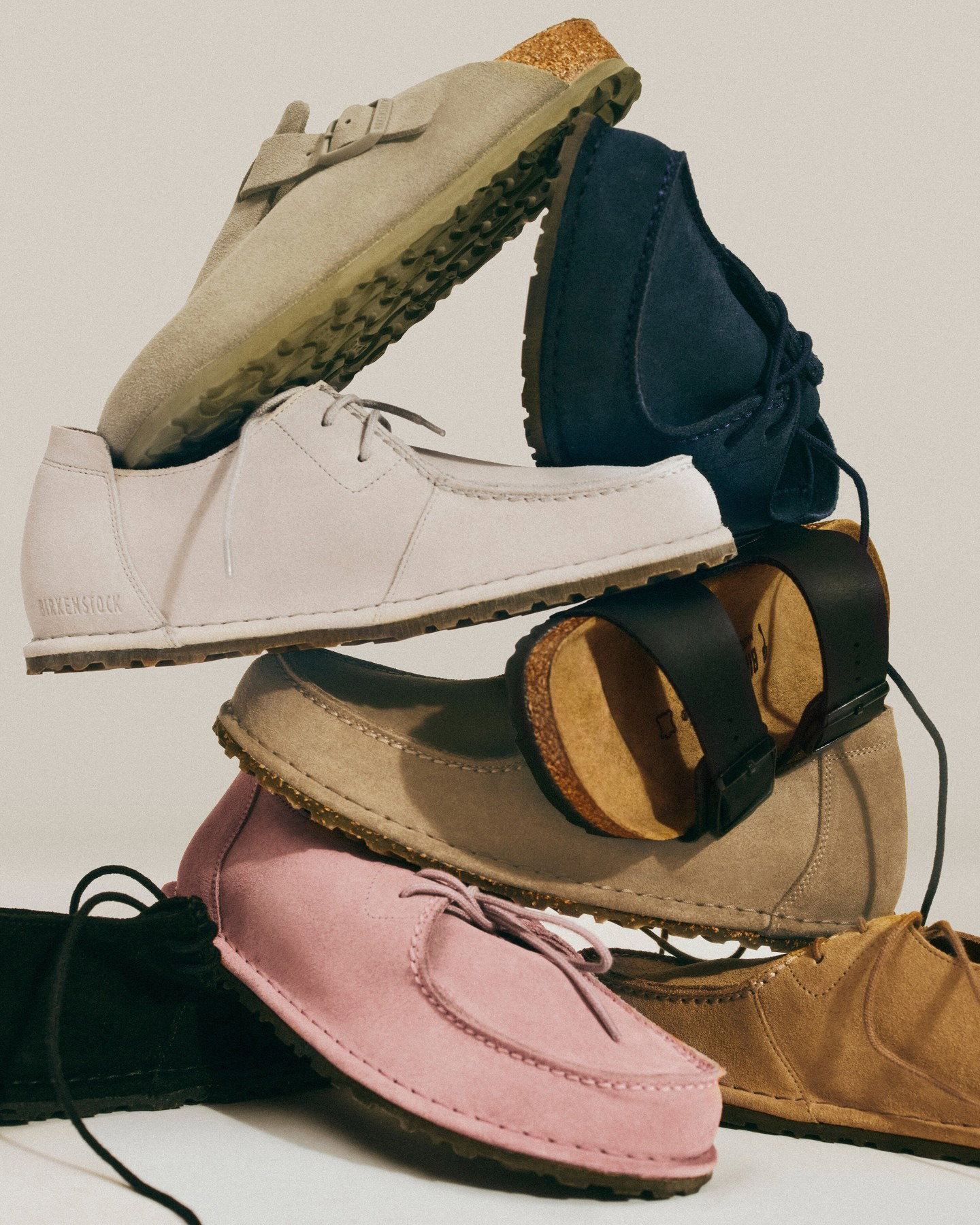 Stack of assorted suede casual shoes and sandals in beige, white, navy, pink and tan with cork footbeds and rubber soles