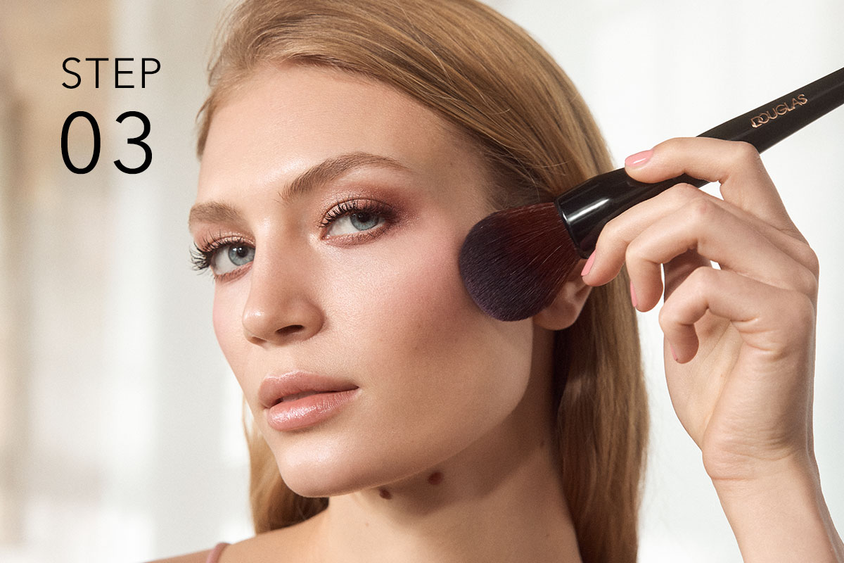 Beauty-Motiv mit „STEP 03“: Person trägt mit einem Pinsel Rouge auf die Wange auf.