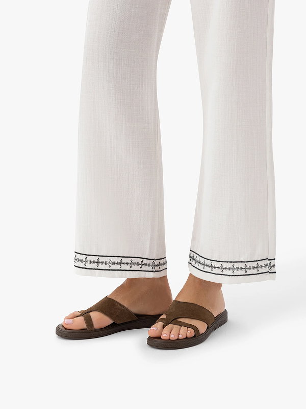 Woman wearing white embroidered trousers and brown sandals on white background