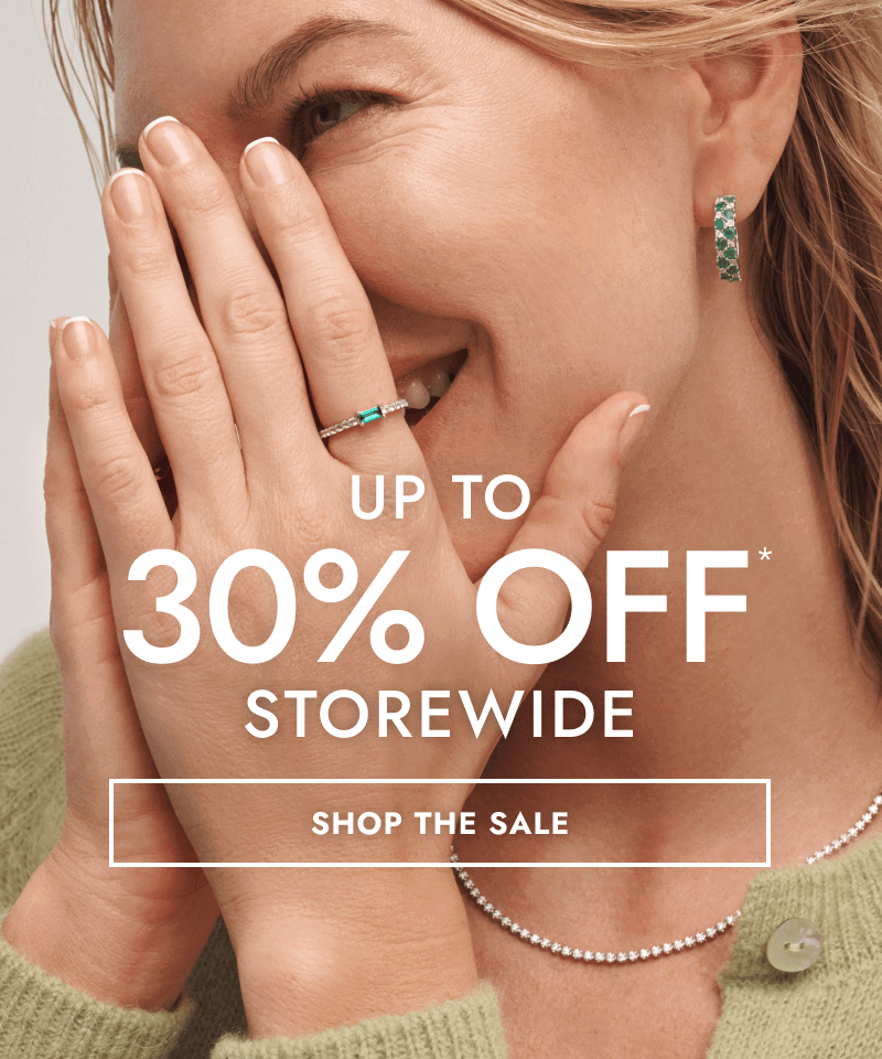 Woman wearing diamond tennis necklace, emerald earrings and ring. Up to 30% Off storewide. Click shop the sale.