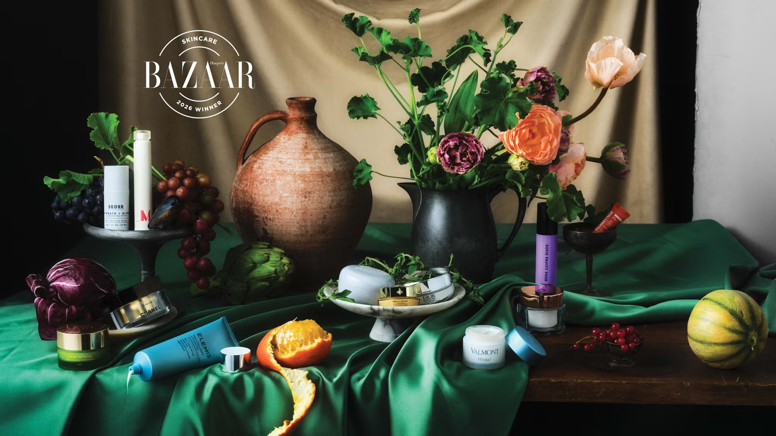 arrangement of skincare products, flowers, and fresh produce on a silky green cloth