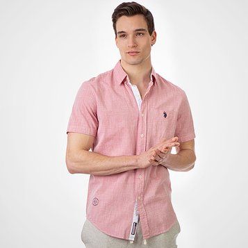 Man wearing pink short-sleeve button-up shirt with small embroidered logo, paired with gray pants.