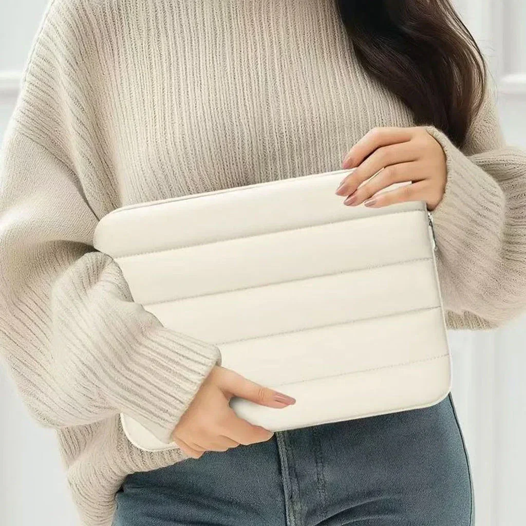 Woman in beige sweater holding white quilted laptop sleeve against her body, paired with blue jeans