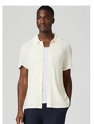 A man wearing a light cream short sleeve button up shirt over a white ribbed tank.