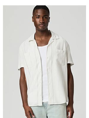 A man wearing a white short sleeve button up shirt with light blue pin stripes over a white ribbed tank.