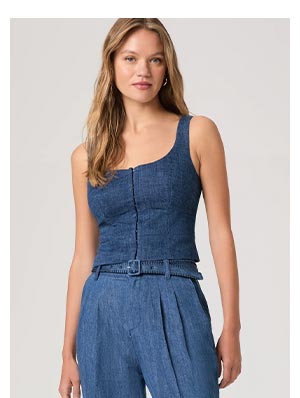 A woman wearing a sleeveless denim top with button front corset style detail.
