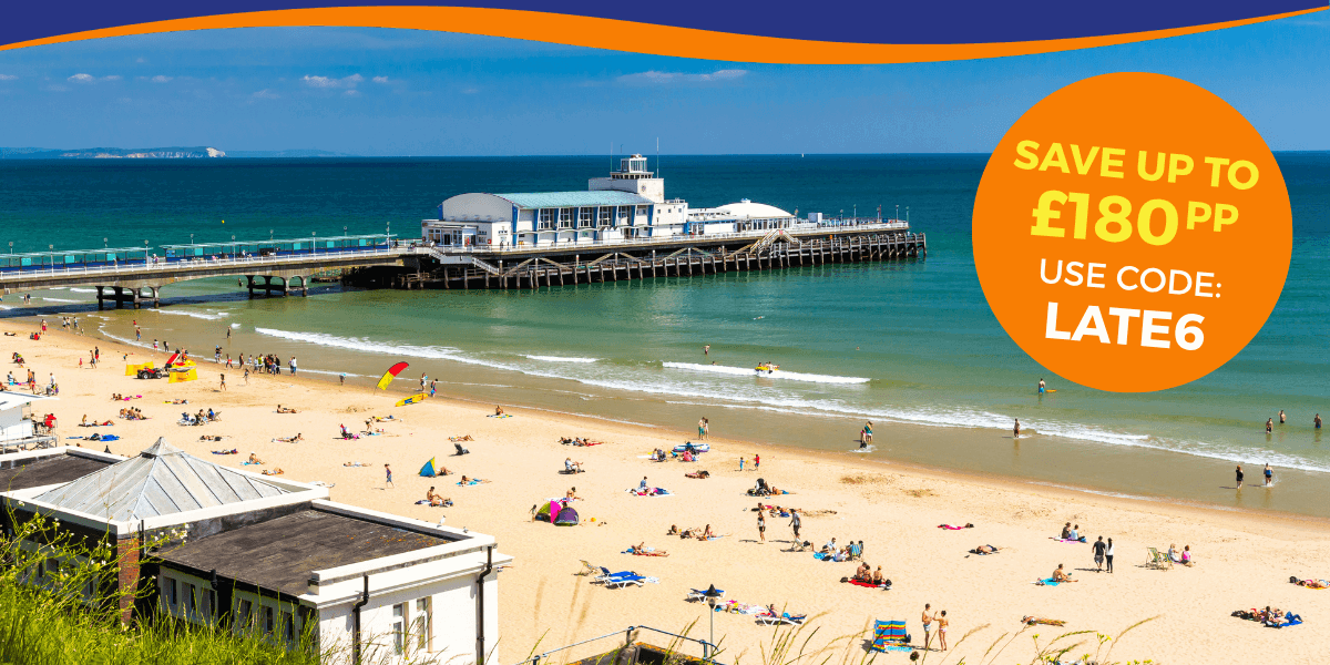 A sunny beach scene with people relaxing on the sand and a pier in the background.