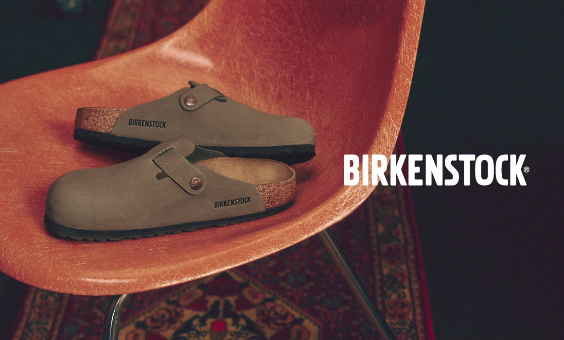 Brown Birkenstock clogs placed on a curved chair with brand logo on the side.