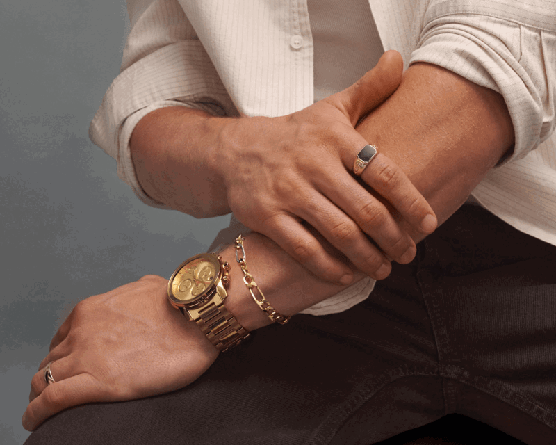 Close-up of a man wearing yellow gold jewelry, including a wedding band, signet ring, watch and chain bracelet.