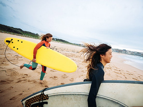 Frauen laufen mit Surfbrettern am Strand entlang.