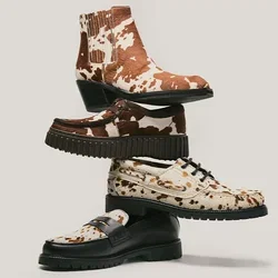Stapel von vier Schuhen mit verschiedenen Mustern, darunter braun-weißer Kuhflecken-Print, Leopardenmuster und einfarbig dunkelbraun, auf hellem Hintergrund.