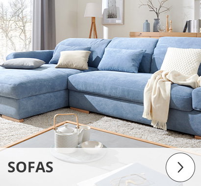 Kategorie Sofas: Ein hellblaues, mit beigen Kissen und einer cremefarbenen Decke dekoriertes Ecksofa steht in einem modern eingerichteten Wohnzimmer mit viel Tageslicht. Auf dem Couchtisch stehen eine Teekanne und eine Tasse. Unten überlagert der Schriftzug „SOFAS“ die Szene.