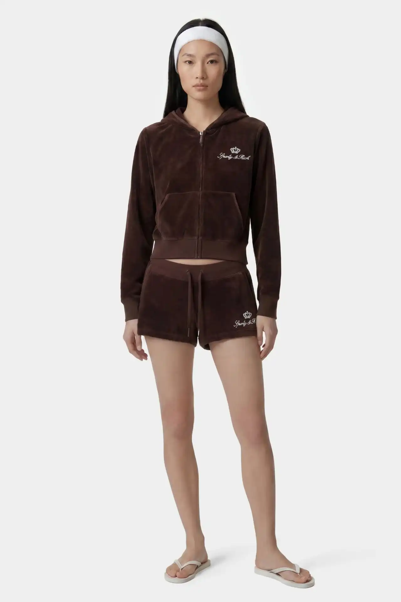 A medium shot shows a woman wearing a brown velour tracksuit consisting of a zip-up hoodie with a crown and 'Juicy Couture' embroidered in white on th...