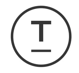 A dark gray circle contains a white uppercase letter T with a horizontal line below it, presented in a flat-lay composition with diffused lighting.