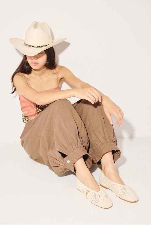 DAISY in Vanilla Crochet styled with a cowboy hat, peach tank top, and pleated brown trousers.