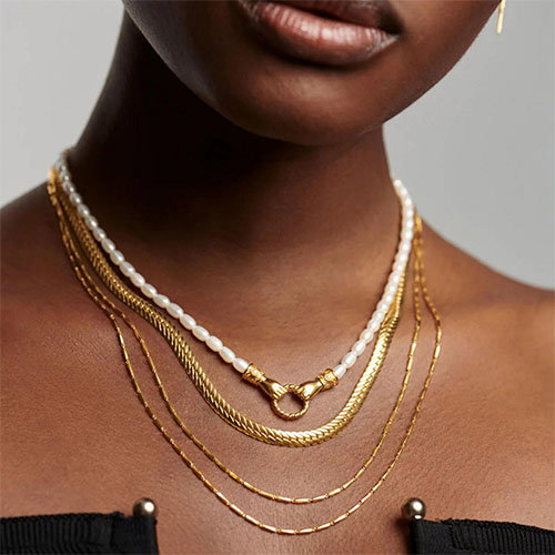 A person wearing layered gold and pearl necklaces with a black top.