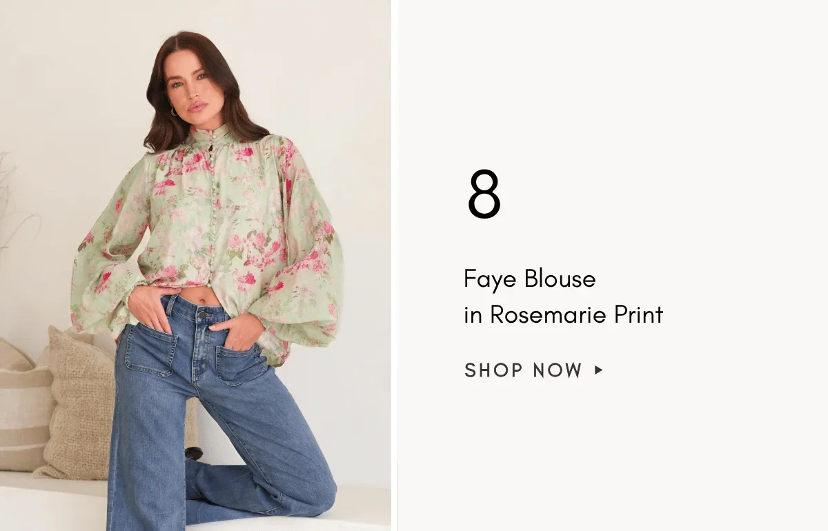 A medium shot shows a woman wearing a light green floral print blouse with puffed sleeves and blue denim jeans, with her hands in her pockets, against...