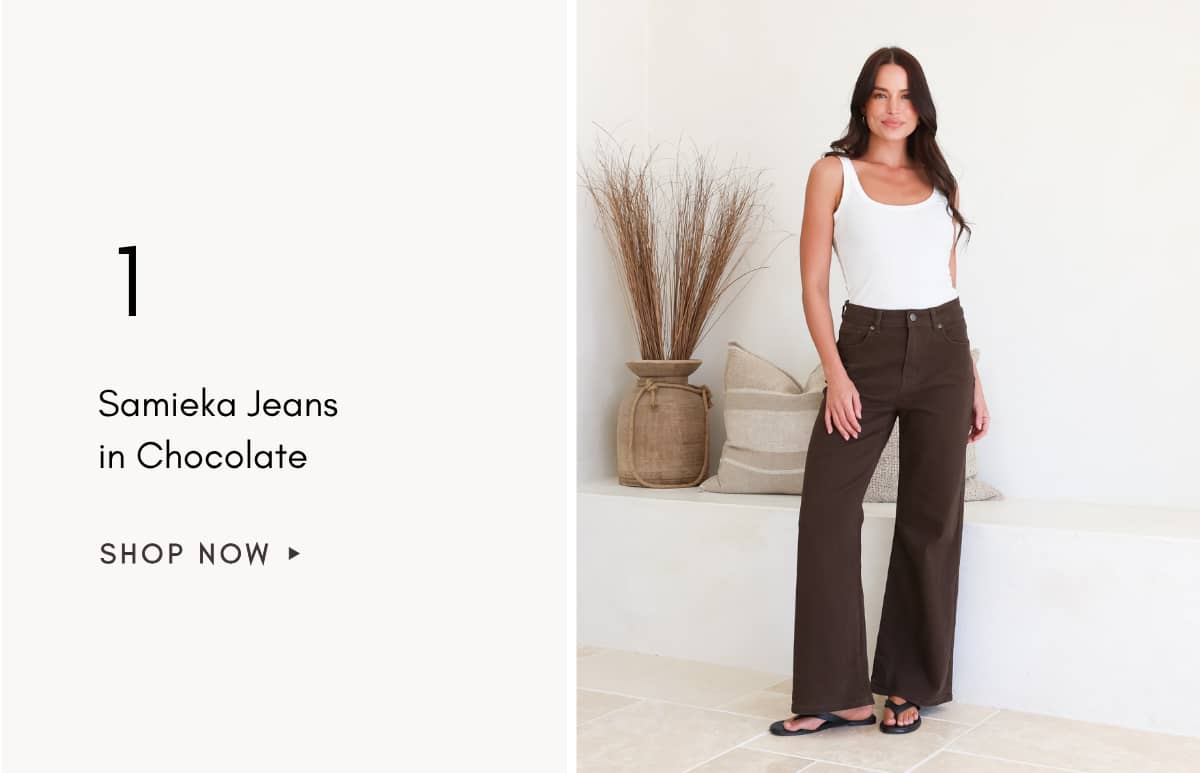 A woman stands in a medium shot wearing a white tank top and dark brown wide-leg jeans, with the text '1 Samieka Jeans in Chocolate SHOP NOW ►' on the...