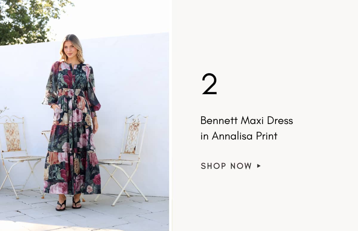 A medium shot shows a woman standing outdoors in front of a white wall and two ornate chairs, wearing a long, dark floral print dress with tiered ruff...