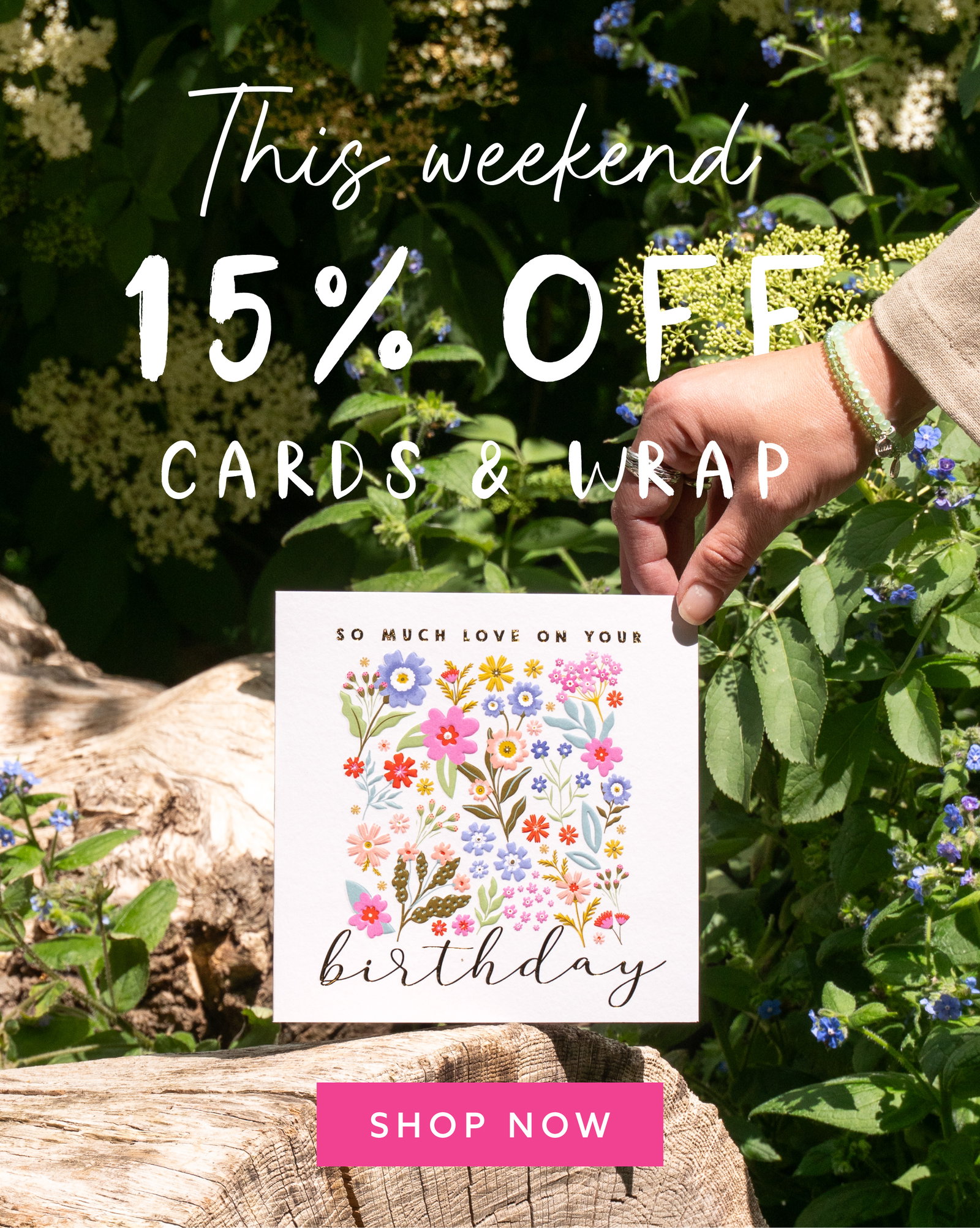 Hand holding a floral birthday card amongst summer greenery with handwritten text reading “This weekend 15% OFF Cards & Wrap” and a bright pink Shop Now button.
