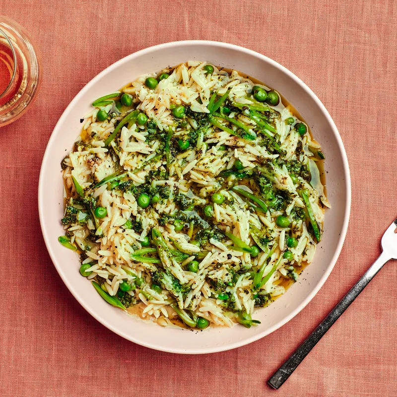 Spring orozotto pasta in a bowl with peas, sliced sugar snaps with a glass of wine.