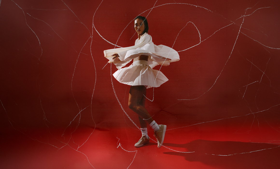 Person in a white outfit dancing against a vivid red background with light streak effects.