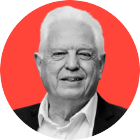 A black and white headshot shows John Simpson looking at the camera. His picture is superimposed in front of a red background. He is wearing a suit with an open-neck shirt.