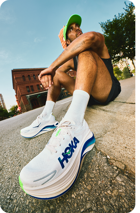 A block of three images: one image shows a man looking to the side, sitting with his elbows resting on his knees, with his shoe in the foreground; one image shows a side view of the Arahi 8 in cobalt blue / neon green; one image shows a side view of the ORA Recovery Slide 3 in neon flame / neon flame.