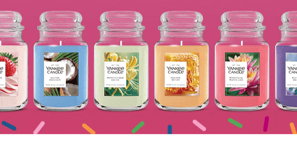 Six Yankee Candle jars in different colors and scents are lined up against a pink background with confetti accents.