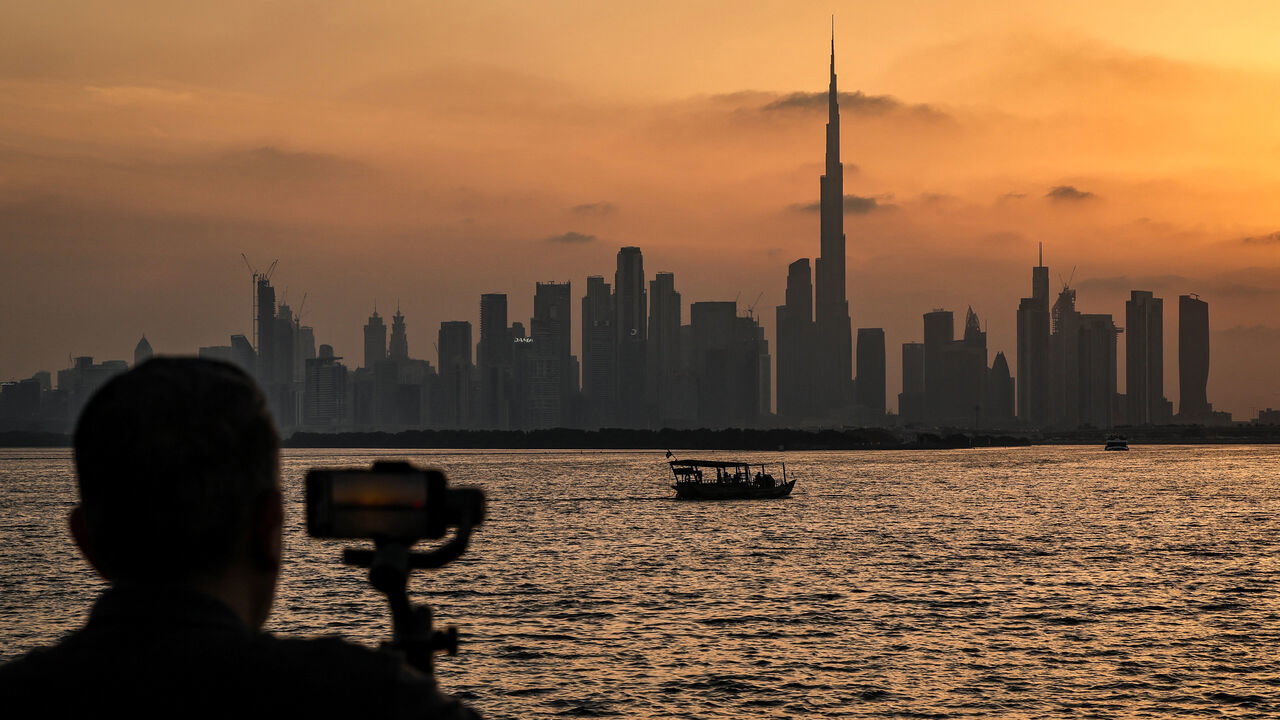 A man stands holding a smartphone in front of the Dubai skyline, with the Burj Khalifa, the world's tallest building, seen from Creek Harbour, UAE.
