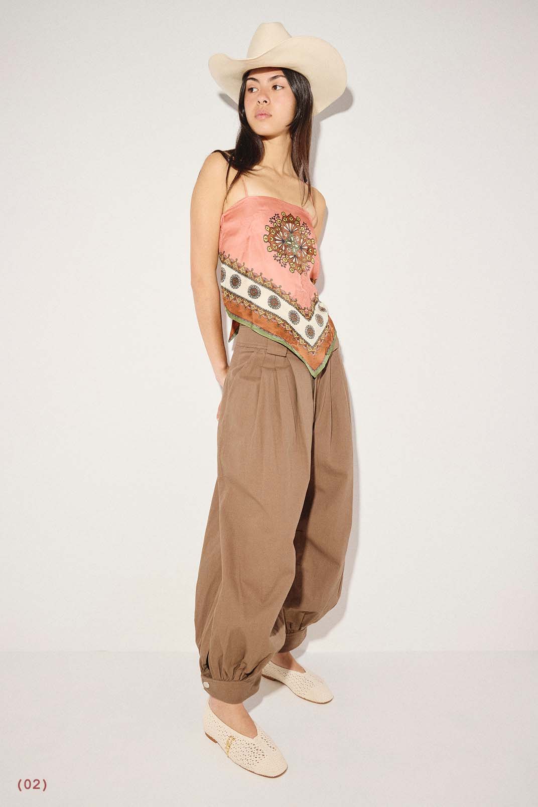 DAISY in Vanilla Crochet styled with a tan cowboy hat, an orange patterned tube top, and brown pleated trousers.