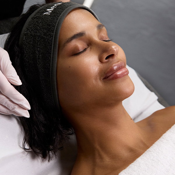A close-up of a woman lying back with eyes closed while receiving a professional treatment.