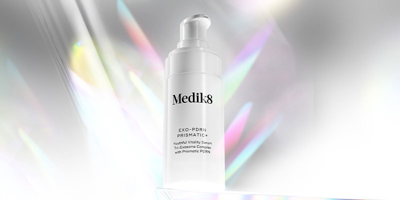 Medik8 Exo-PDRN Prismatic+ Youthful Vitality Serum pump bottle displayed beside a stylised DNA strand with a ‘NEW’ label against a soft iridescent background.