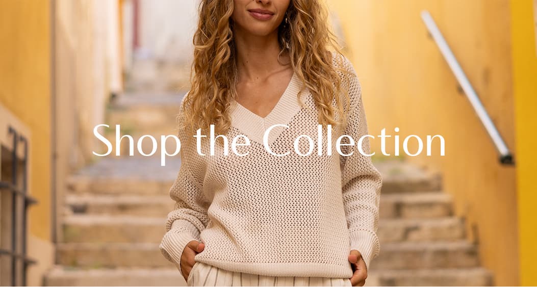 Model wearing a cream open-knit sweater outdoors on stone steps, with overlay text reading “Shop the Collection.”