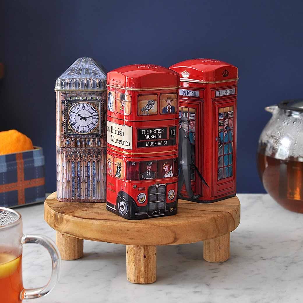 Three tea caddies in the shape of a red telephone box, a London bus, and Big Ben are displayed on a marble countertop. – Shop Food and Drink.