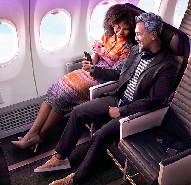 Couple laughing and smiling at each other on a plane in an Economy X seat