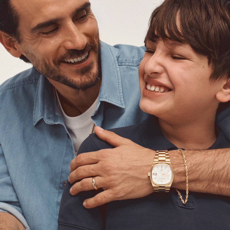 Man wearing gold watch, bracelet, and ring while embracing smiling child.