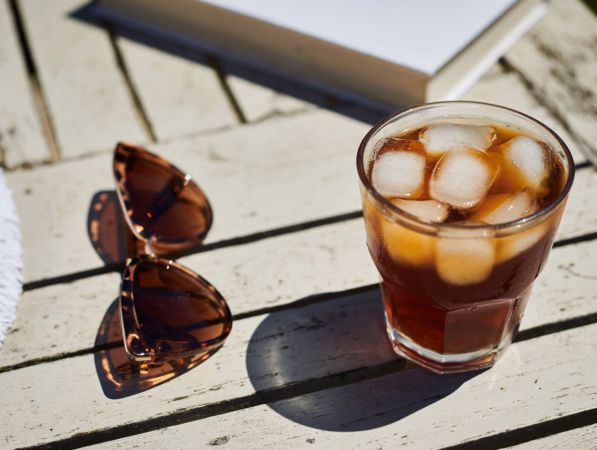 Glass of Peet's iced coffee next to a pair of sunglasses on a wood table outside