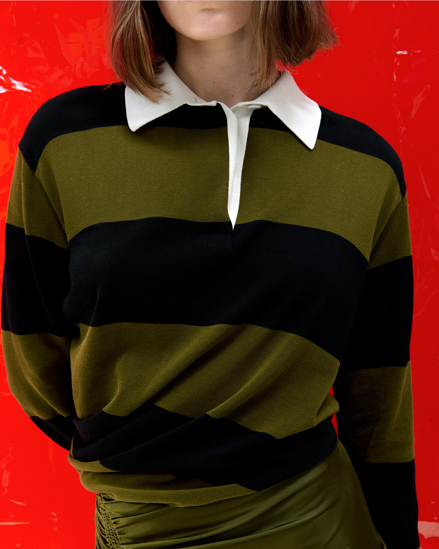 Cropped image of model standing against red vinyl background wearing the Corinna Top in Cotton Stripe in Black Multi with the Naia Skirt in Viscose Satin Jersey in Moss
