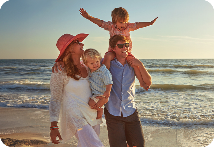 Fröhliche Familie mit zwei Kindern läuft gemeinsam am Strand bei Sonnenuntergang.