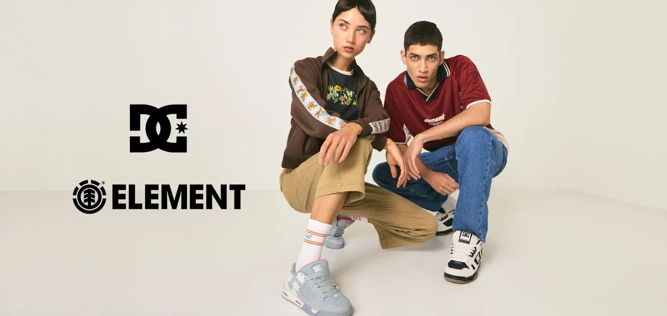 Dos jóvenes agachados sobre un suelo claro contra una pared simple, vistiendo ropa casual y zapatillas, mirando hacia adelante con expresiones serias.