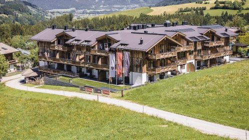 Gondel im Vordergrund des Hotel sowie einer Bergkette im Sommer