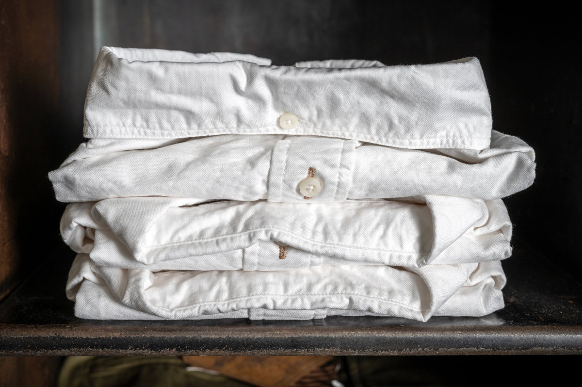 Three pairs of Bills Khakis white standard fit shirts site folded in an industrial shelf