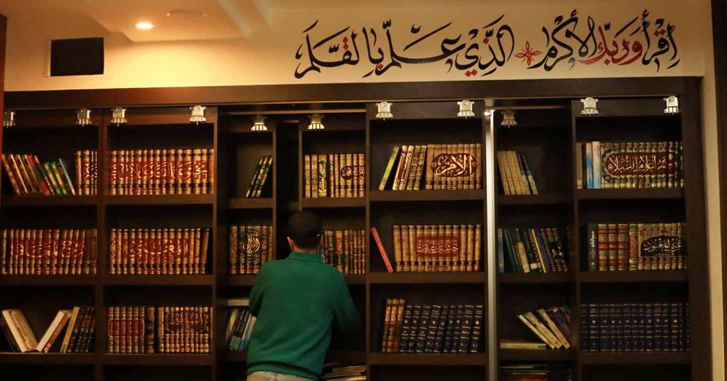 A person in a green shirt in front of a wall of shelves filled with books