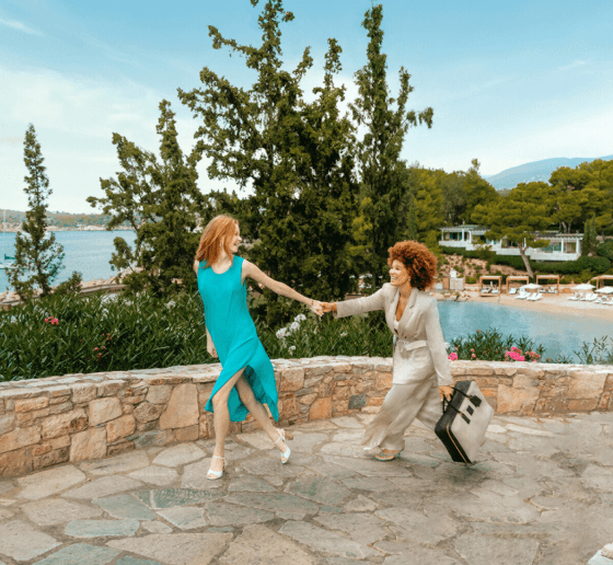 Two people holding hands, strolling by the seaside with trees around them.
