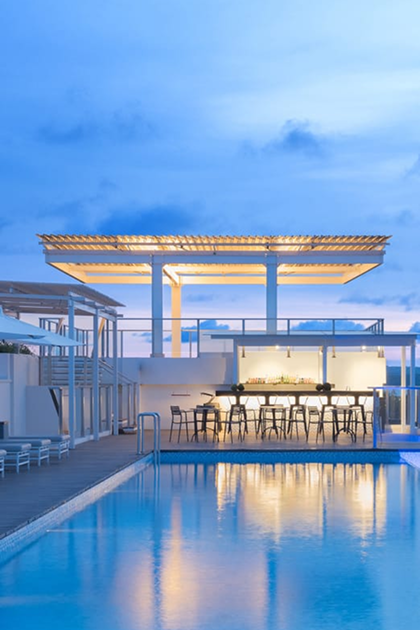 A pool just after sunset with a lit seating area and covered patio at one end.