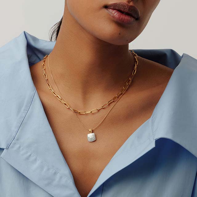 Person wearing layered gold chain necklaces and a blue blouse.