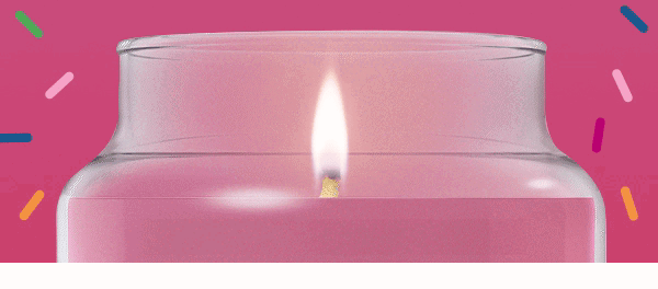 Lit candle in a glass jar with colorful confetti-like accents on pink background.